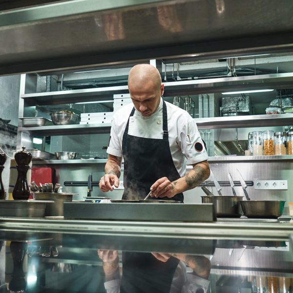 Professional chef. Famous young chef in black apron working at his modern restaurant kitchen