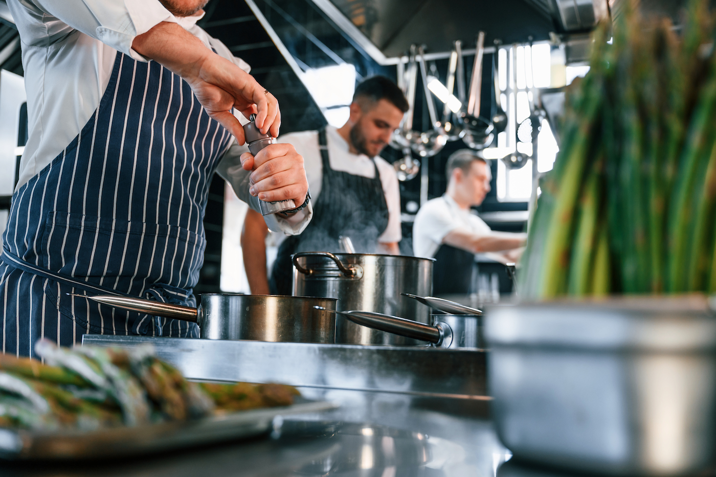 Boiling and adding ingredients. Kitchen workers is together preparing the food