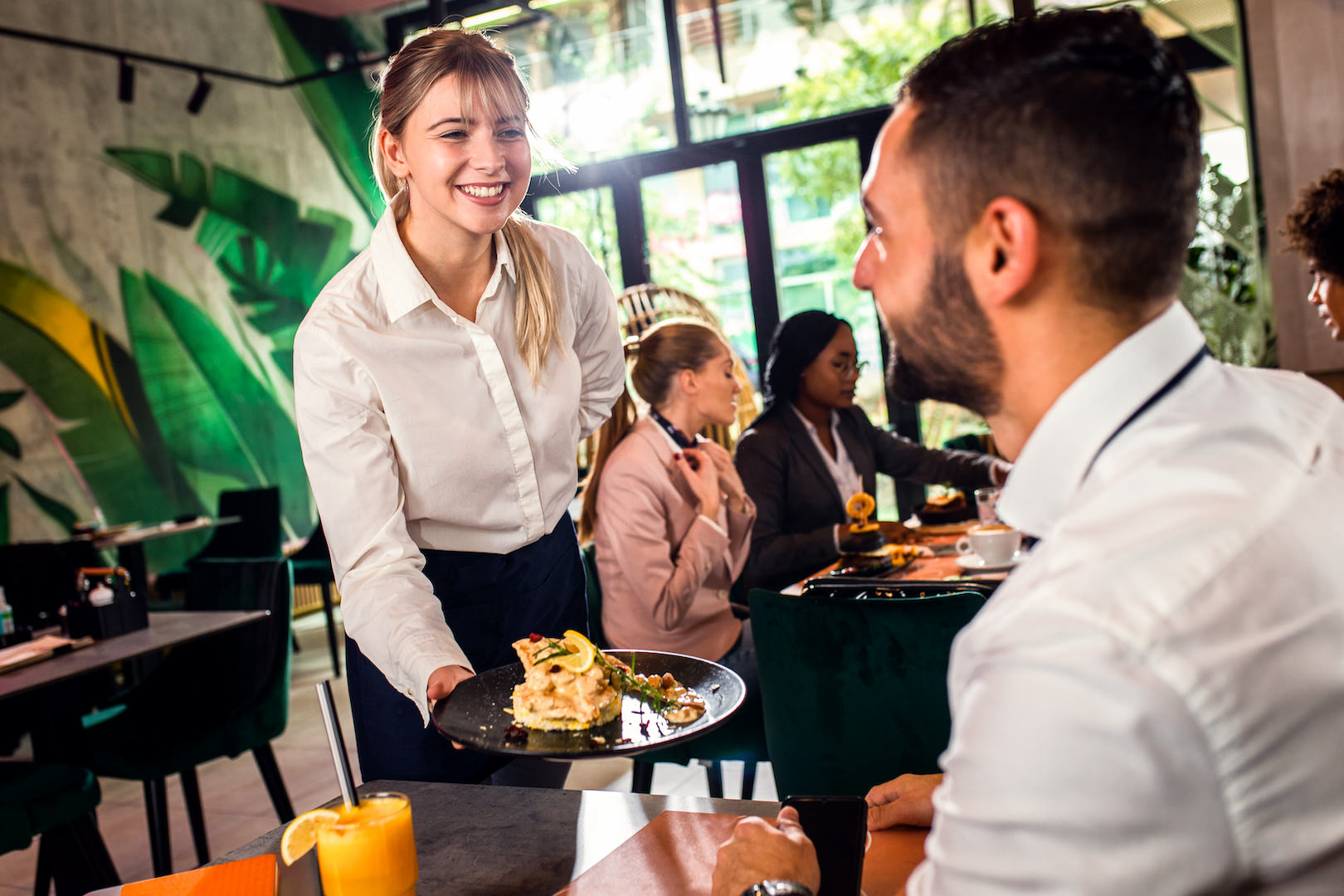 Smiling waitress serving meal to young businessman in restaurant.