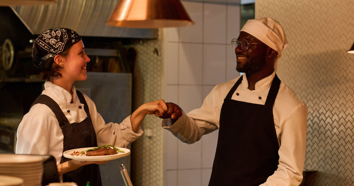Two happy young intercultural kitchen workers giving each other punch bump