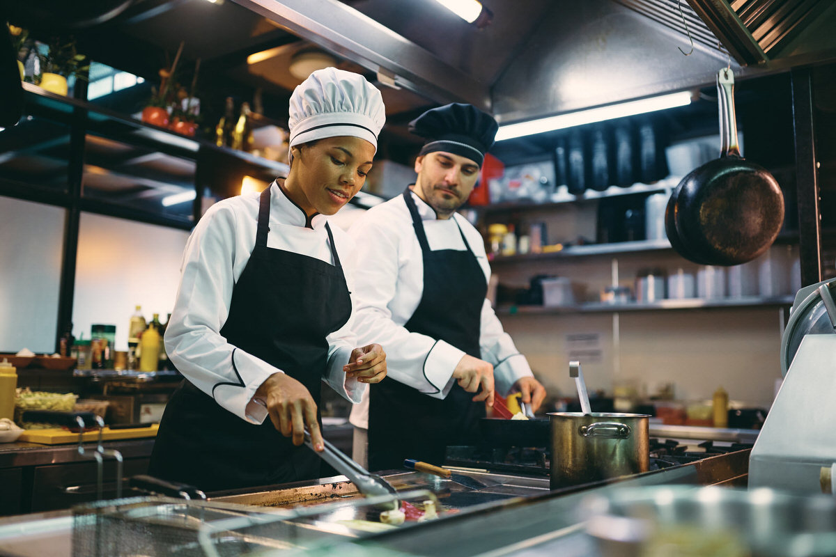 Black chef and her male coworker preparing food while working in a restaurant.