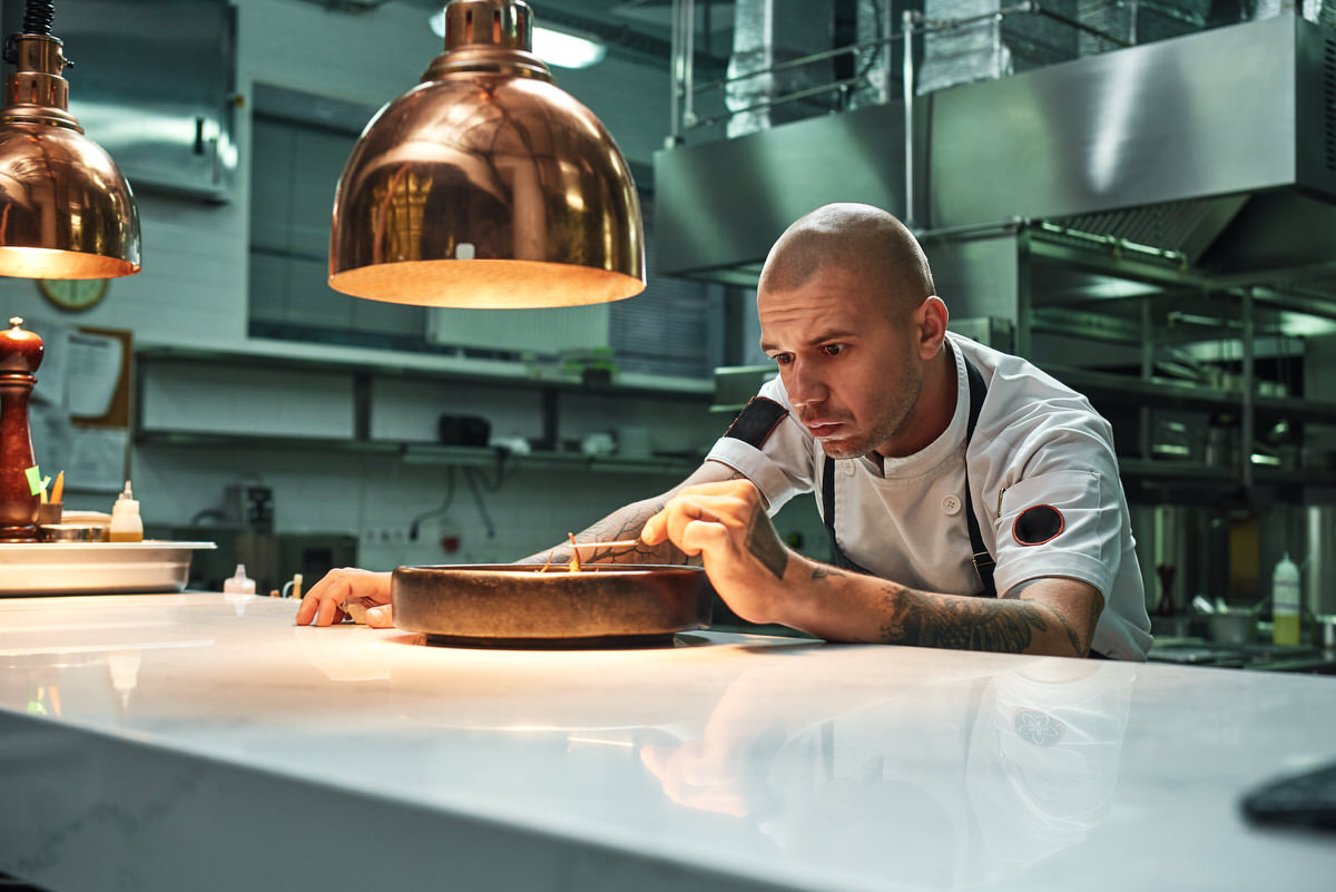 Delicate work. Confident chef decorating delicious chocolate cake while standing in a restaurant kitchen.