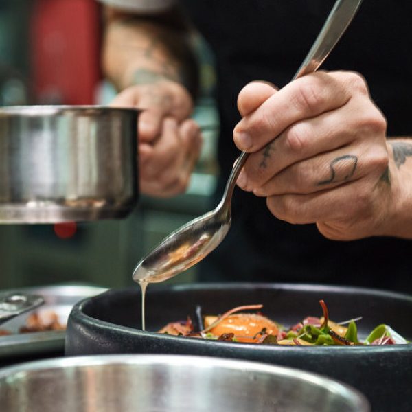 Secret recipe. Close up photo of chef hands with several tattoos adding a sauce to italian pasta Carbonara.