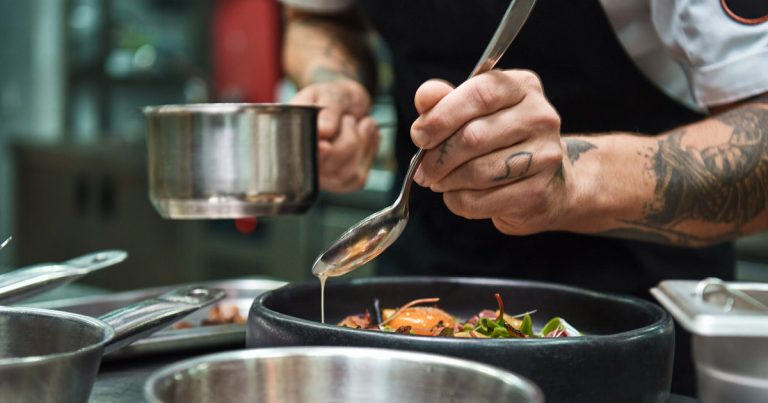 Secret recipe. Close up photo of chef hands with several tattoos adding a sauce to italian pasta Carbonara.