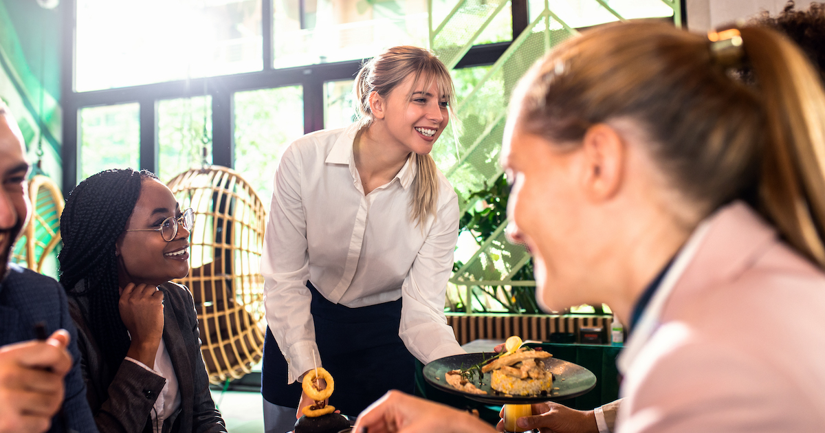 Smiling waitress serving meal to group of business people in restaurant.