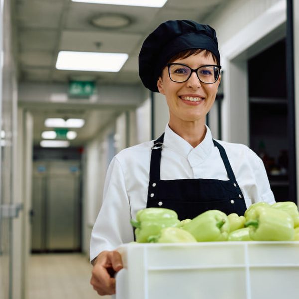 Happy female chef carrying fresh vegetables from the pantry and looking at camera.