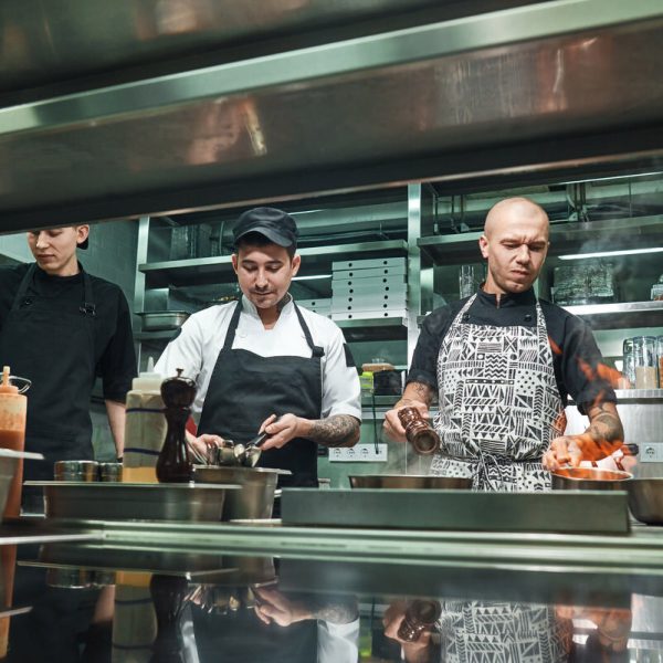 Professional team. Young brutal chef in uniform flambeing in a professional kitchen.