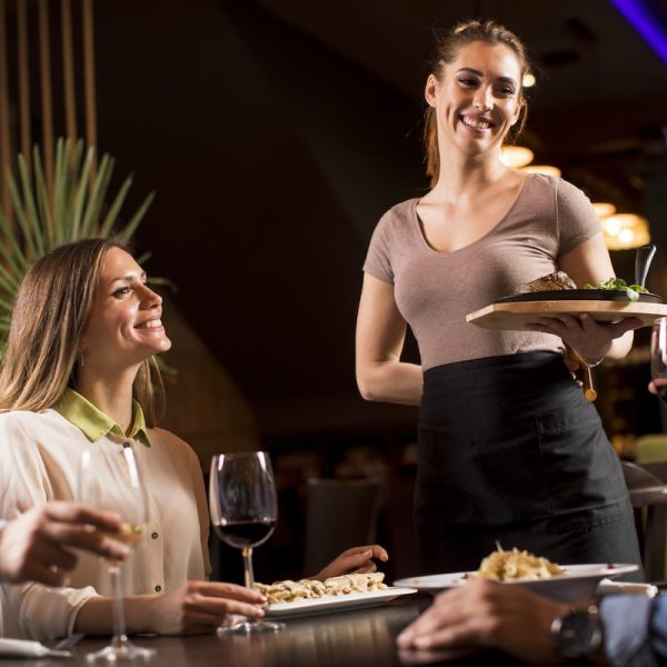 Waiter woman serving group of friends with food in the restaurant