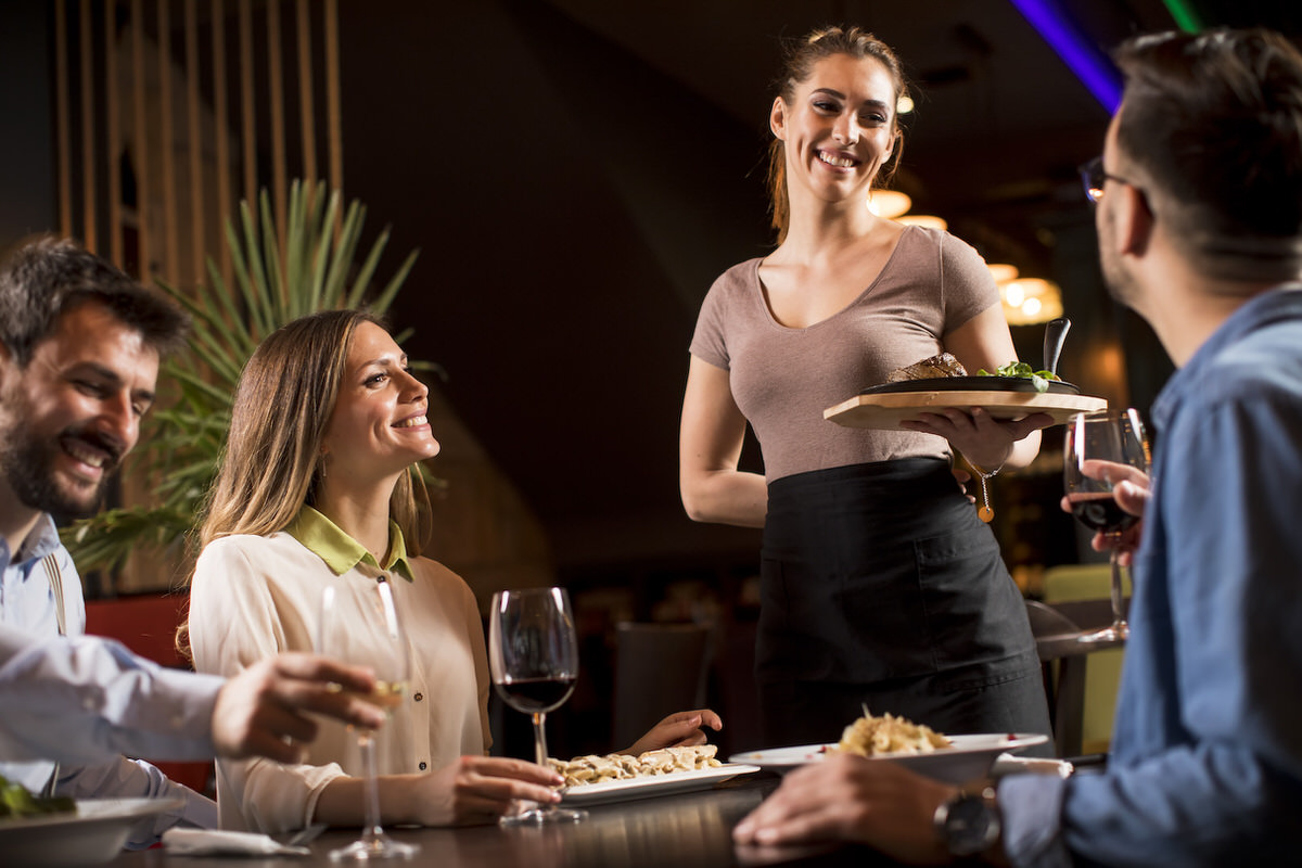 Waiter woman serving group of friends with food in the restaurant