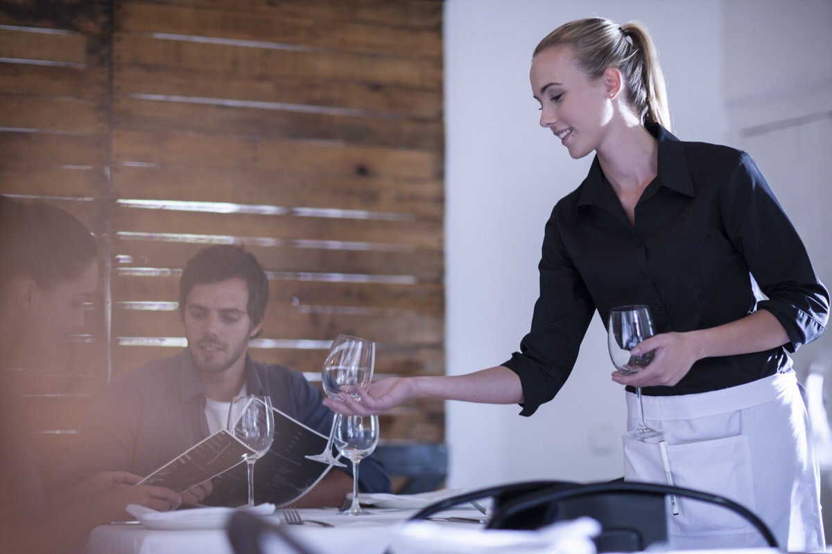 Waitress setting table with wine glass for customers