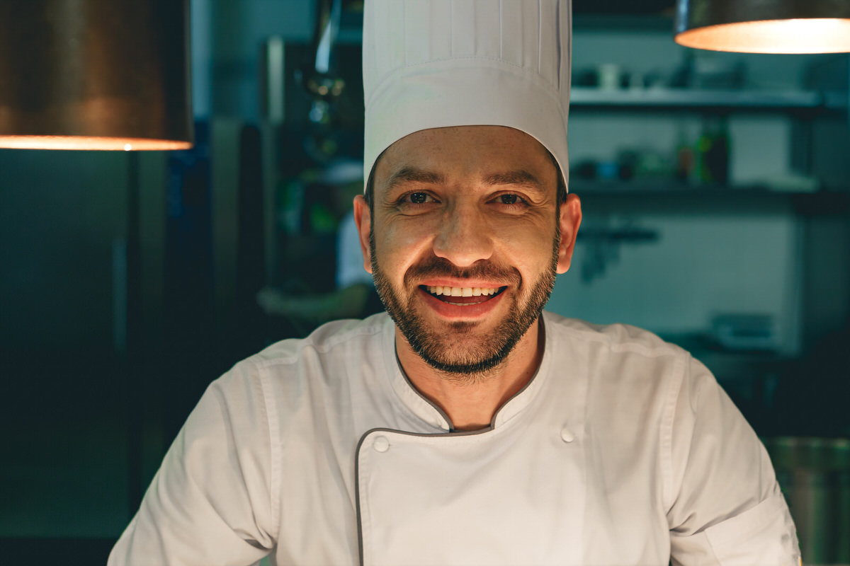 Portrait of smiling male chef in uniform standing on kitchen of restaurant
