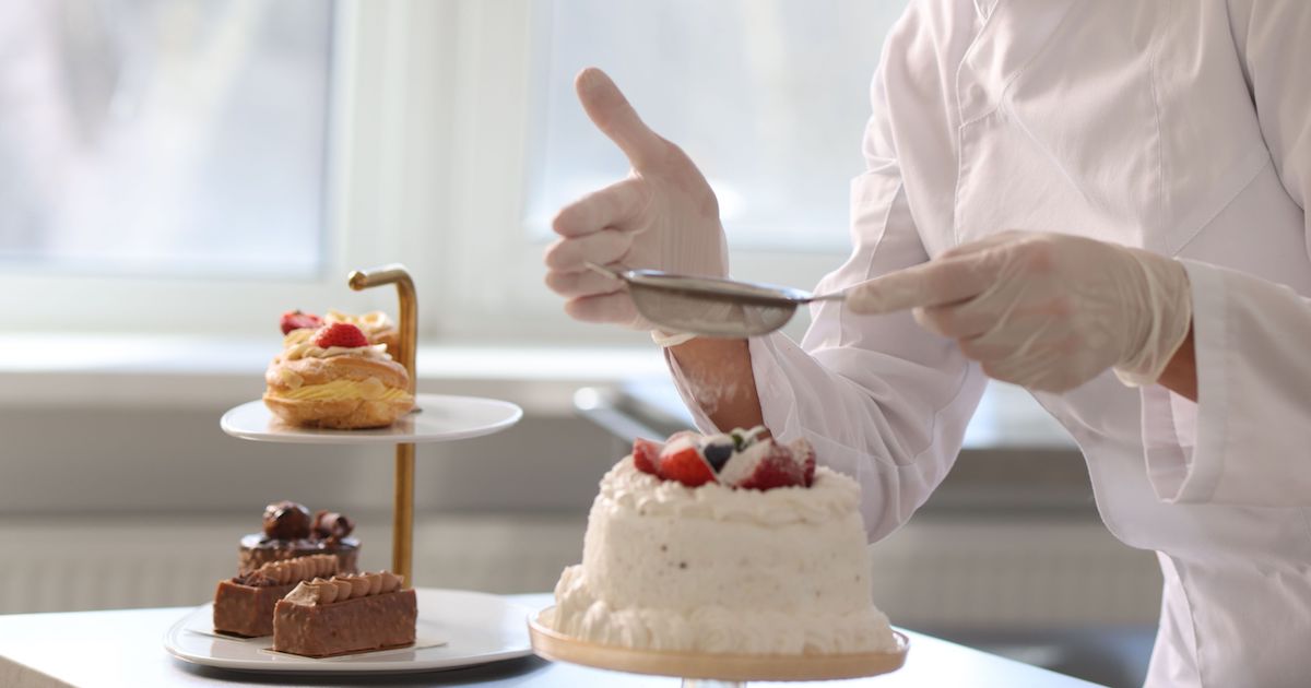 Confectioner sprinkling powdered sugar onto cake in kitchen