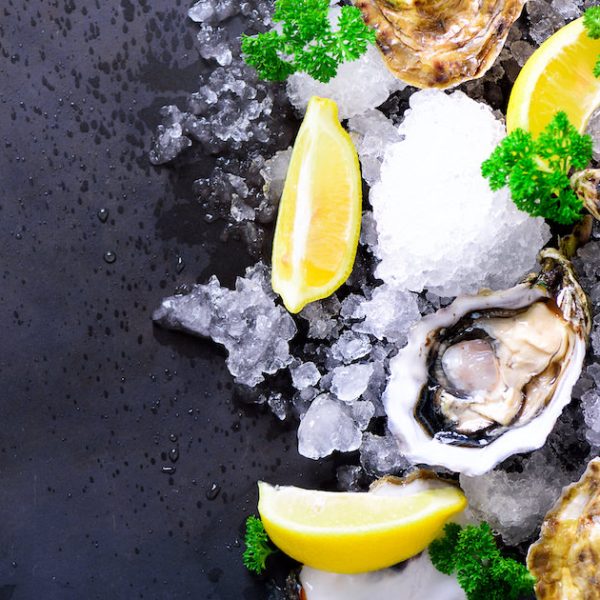 Fresh opened oysters, lemon, herbs, ice on dark metal background. Top view, copy space