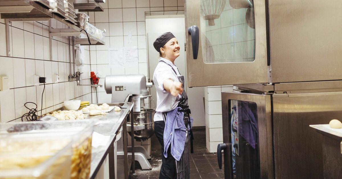 Side view of happy female chef looking in oven at commercial kitchen